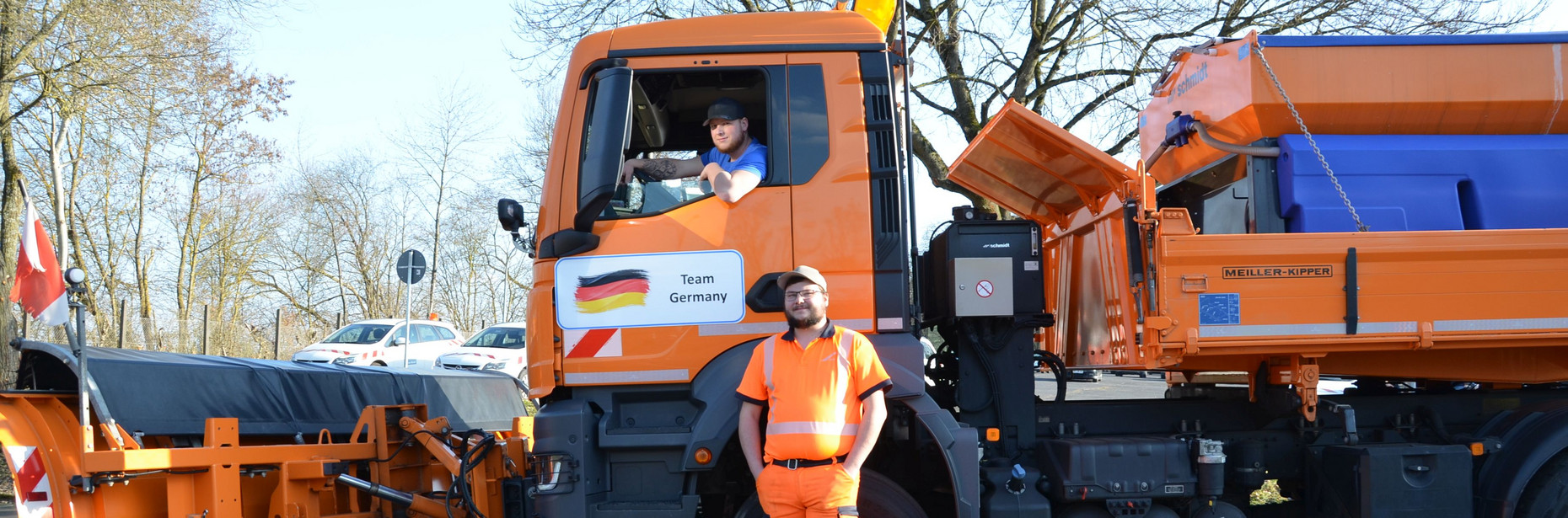 Ein LKM mit montiertem Schneepflug. Ein Mann lehnt sich aus dem Fahrerdfenster, ein anderer steht darunter mit dem Rücken an den LKW gelehnt.