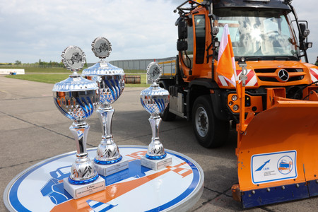 Im Hintergrund ein Unimog mit Schneepflug, im Vordergrund die drei Siegerpokale